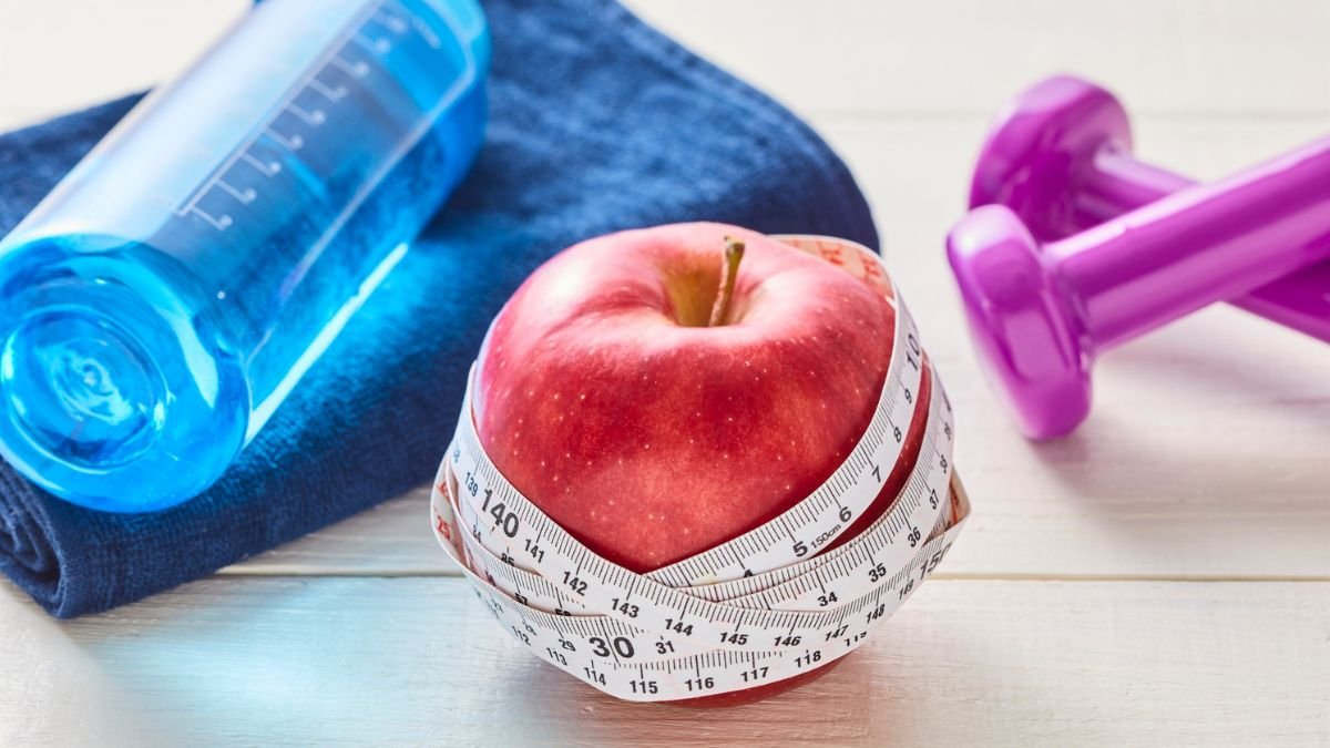 Ein roter Apfel mit einem Maßband, Wasserflasche und Hanteln auf einem Tisch.