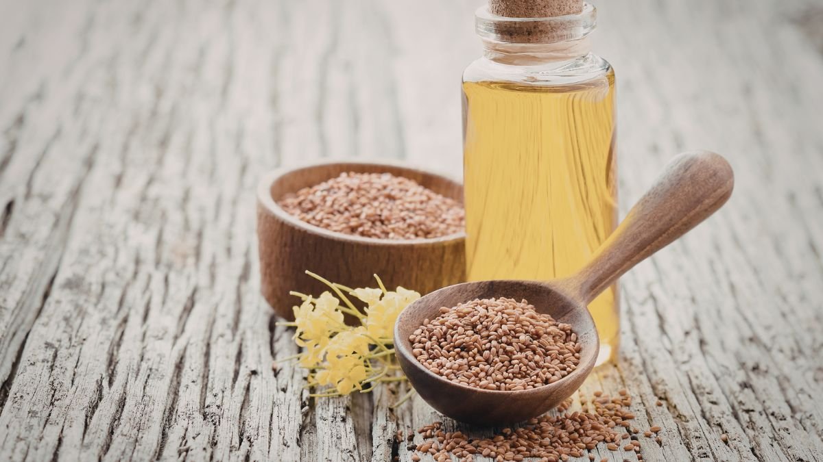 Eine Flasche Leinöl neben einer Schale mit Leinsamen auf einem Holzuntergrund.
