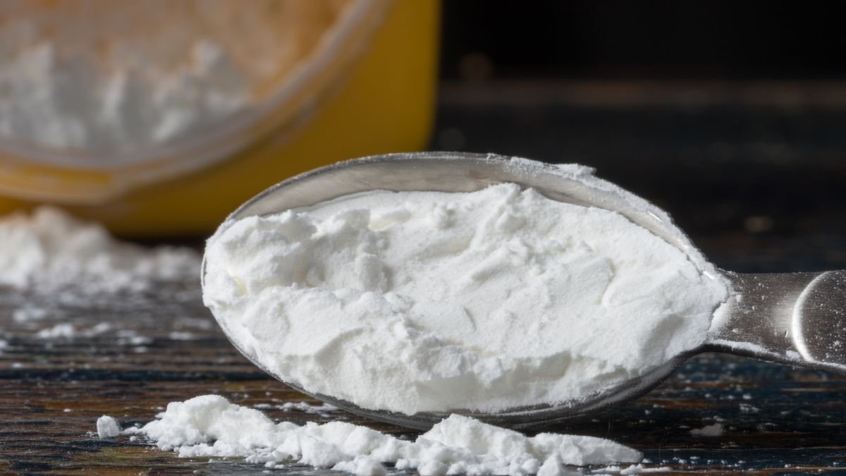 Ein Löffel mit feiner Maisstärke auf einem Holzuntergrund.