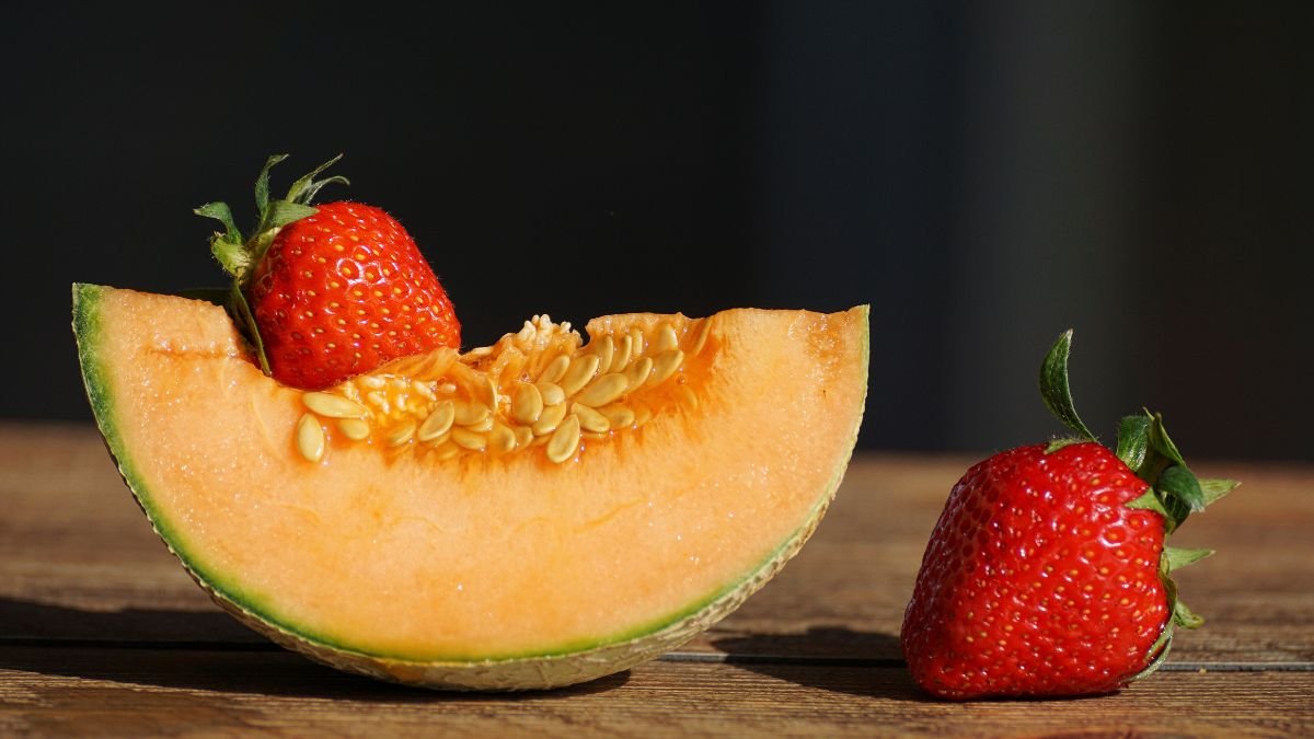 Ein Stück Melone mit frischen Erdbeeren auf einem Holztisch.