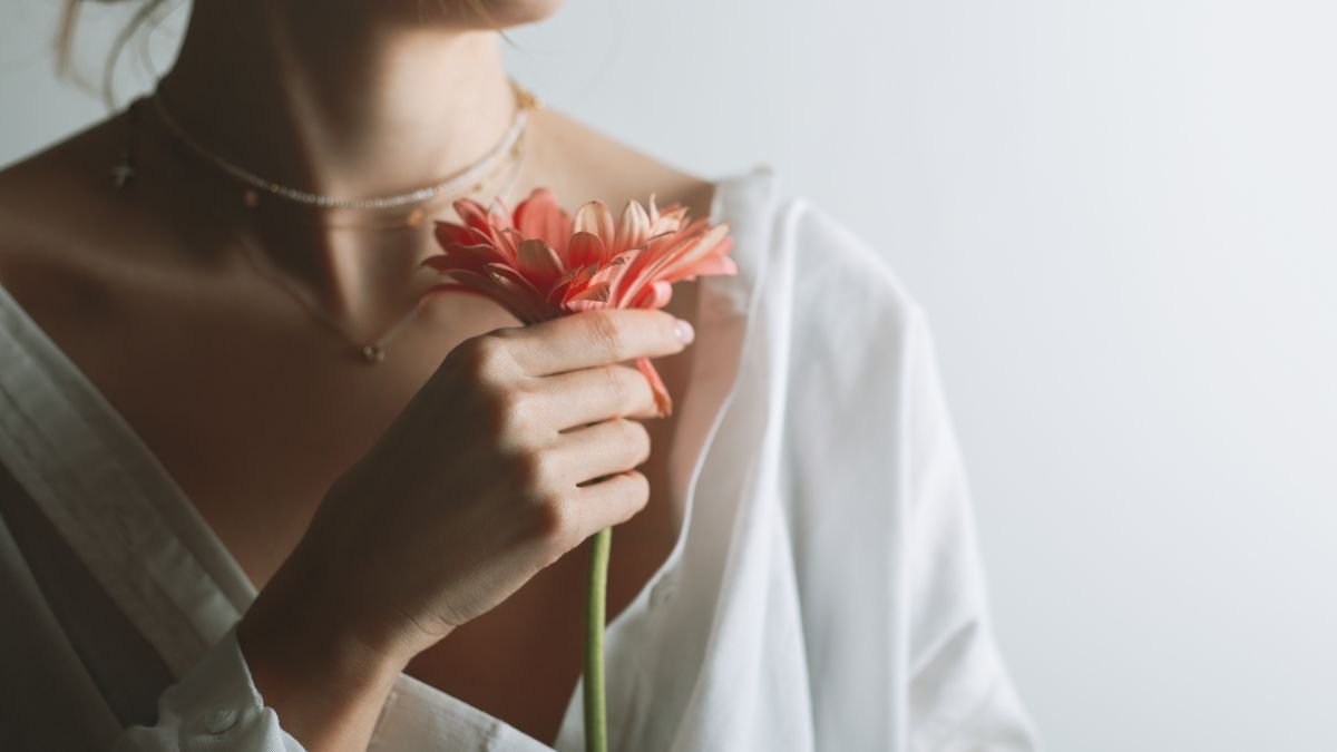 Eine Frau hält eine pinke Blume in der Hand, trägt eine weiße Bluse.