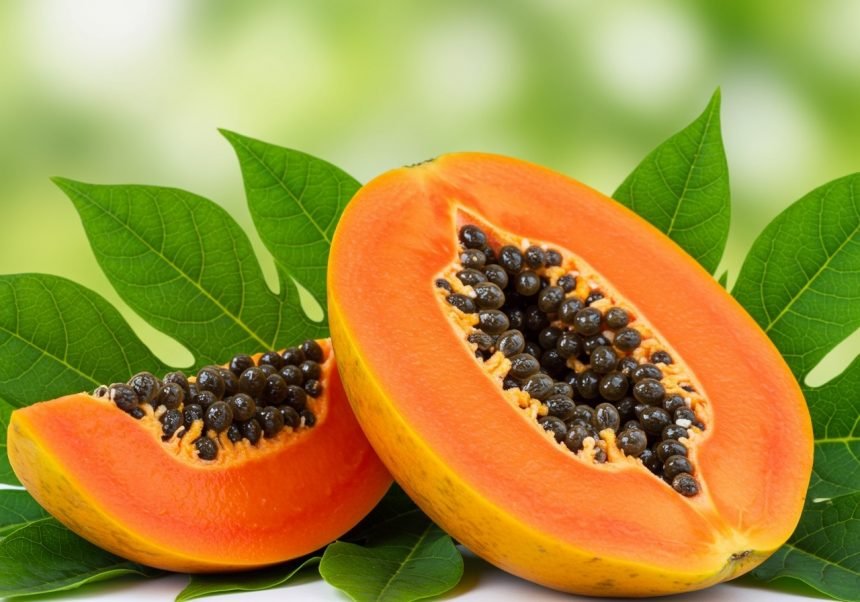 Eine frische Papaya mit schwarzen Kernen, auf grünen Blättern präsentiert.