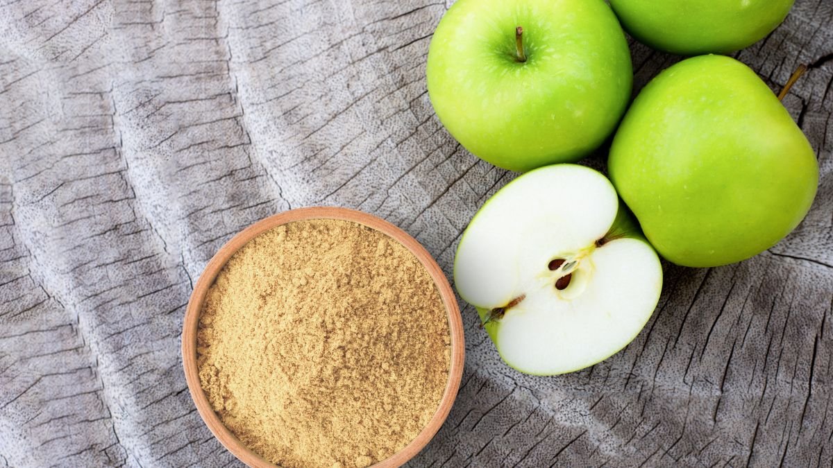 Eine Schüssel mit Pektinpulver neben frischen grünen Äpfeln auf Holz.