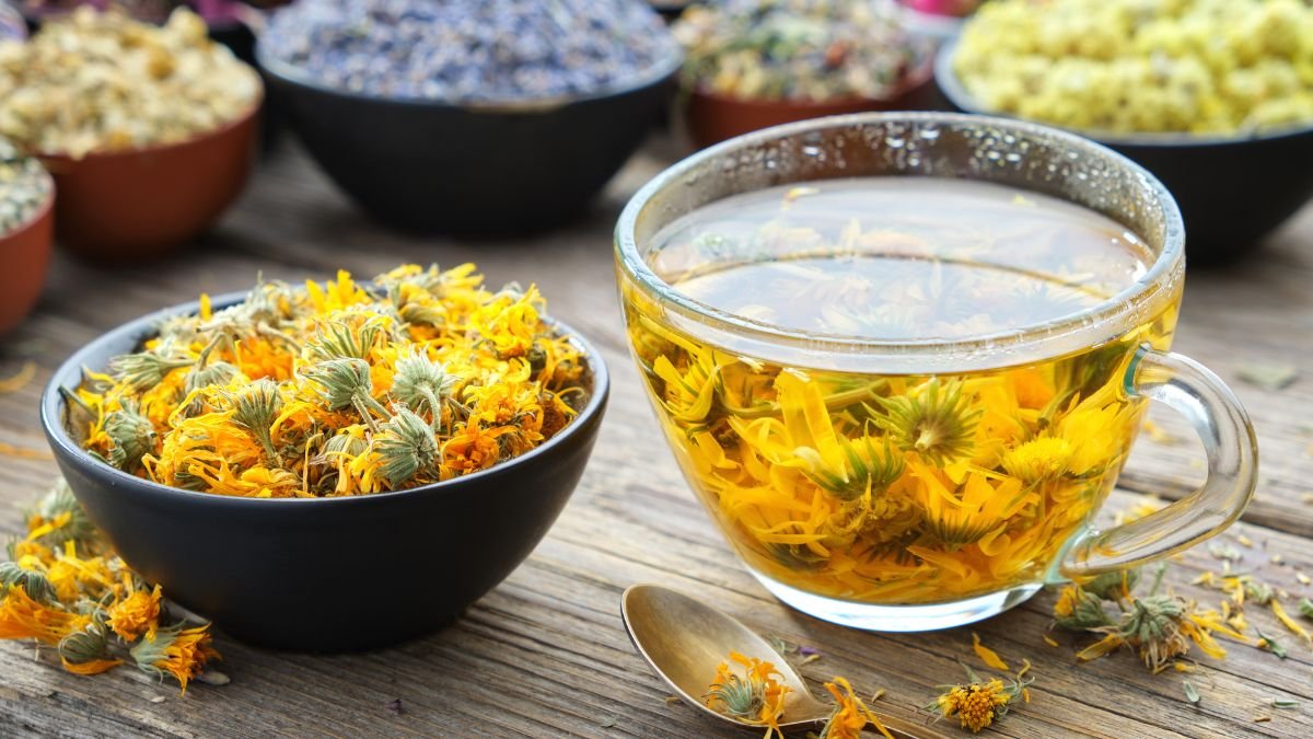 Eine Tasse Ringelblumentee mit getrockneten Ringelblumenblüten daneben.