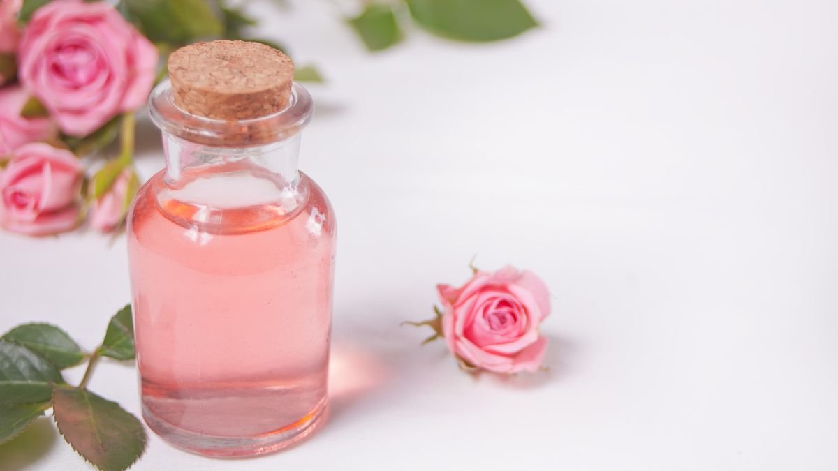 Eine Flasche mit rosa Rosenwasser steht neben frischen Rosenblüten.