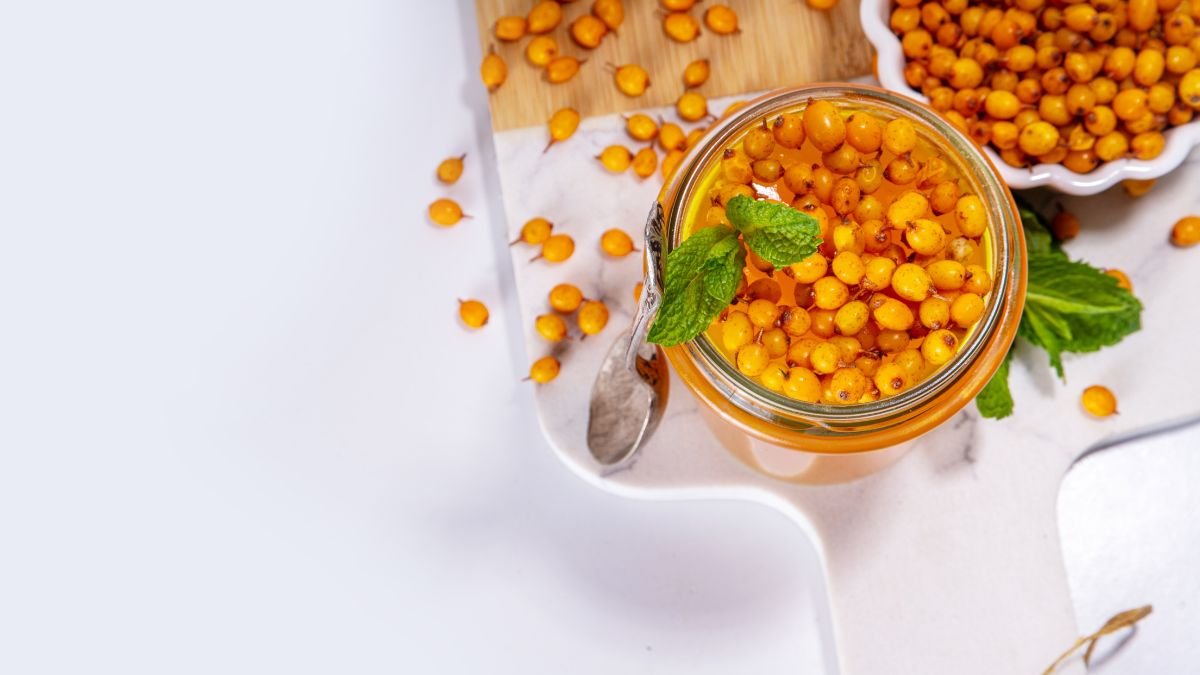 Ein Glas mit Sanddornbeeren und frischer Minze auf einem Tisch.