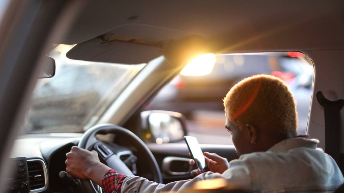 Eine Person sitzt im Auto und nutzt ihr Smartphone während der Fahrt.