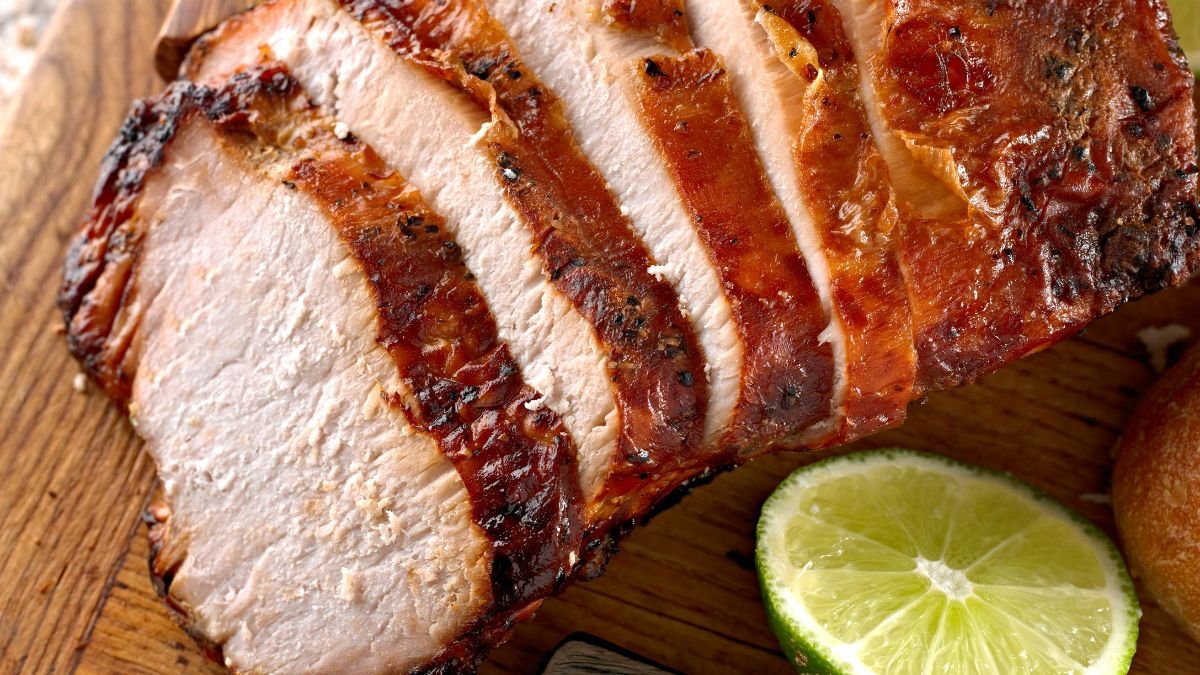 Saftiges, gegrilltes Schweinefleisch auf einem Holzbrett, mit Limettenscheiben.