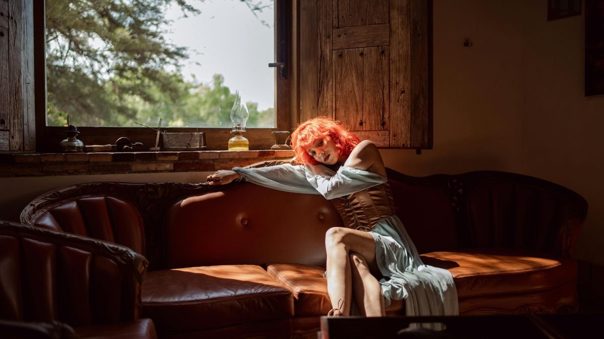 Eine Frau mit rotem Haar sitzt entspannt auf einer Couch und genießt das Licht.