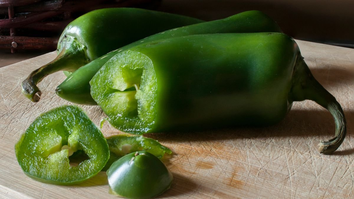 Zwei frische Jalapeños, einer halbiert und in Scheiben geschnitten, auf einem Holzbrett.