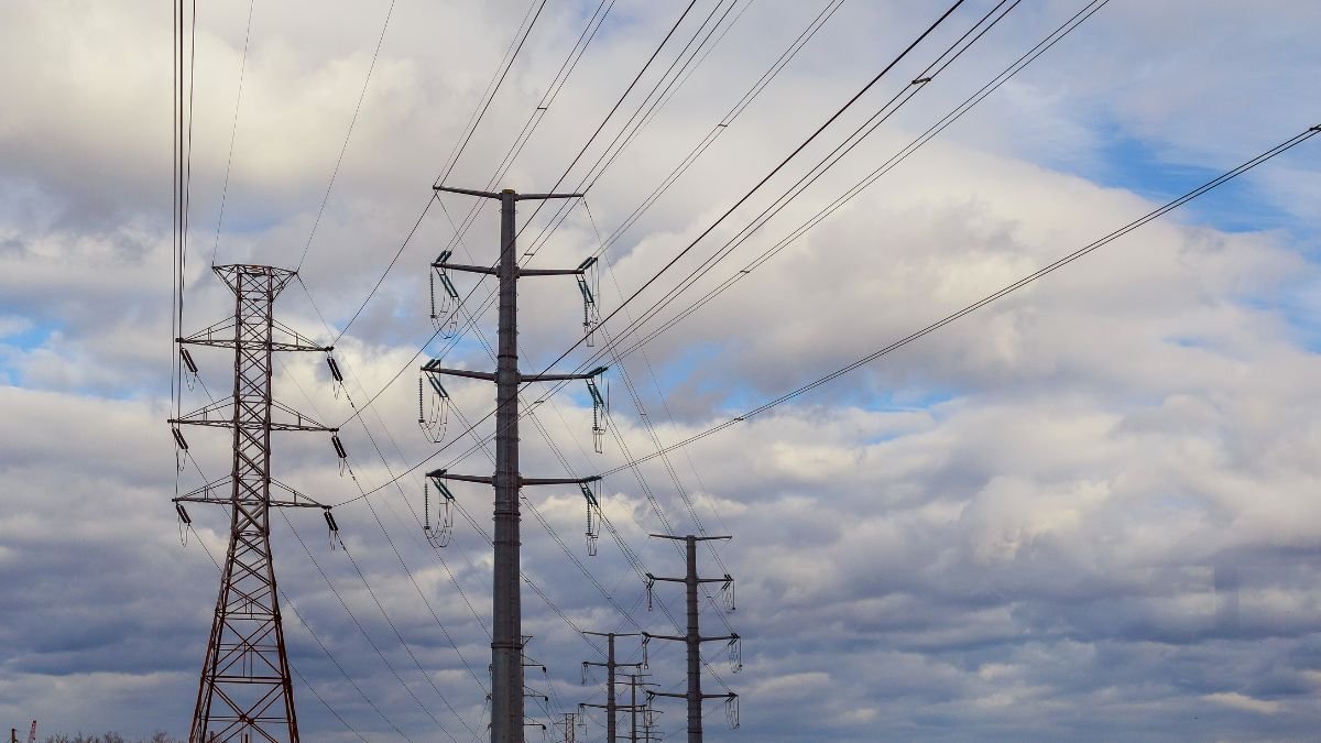 Hochspannungsleitungen ragen in den Himmel unter einem bewölkten Himmel.