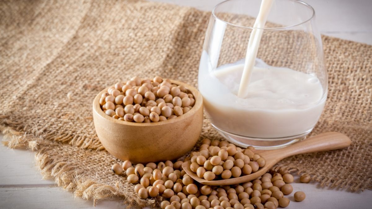 Eine Schüssel mit Sojabohnen und ein Glas Sojamilch auf einem Tisch.