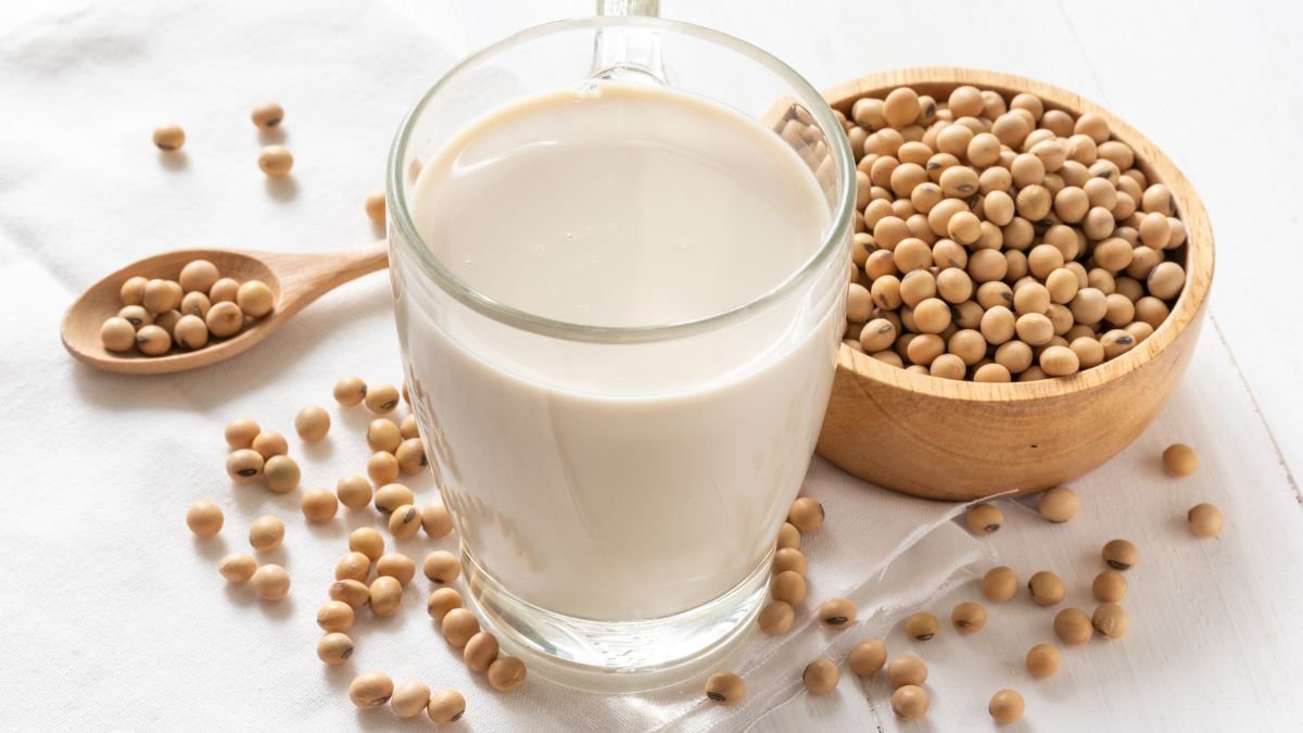 Ein Glas Sojamilch steht neben einer Schale mit Sojabohnen auf einem Tisch.