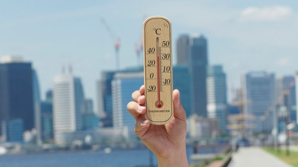 Ein Holzthermometer wird vor einer modernen Stadtlandschaft gehalten.