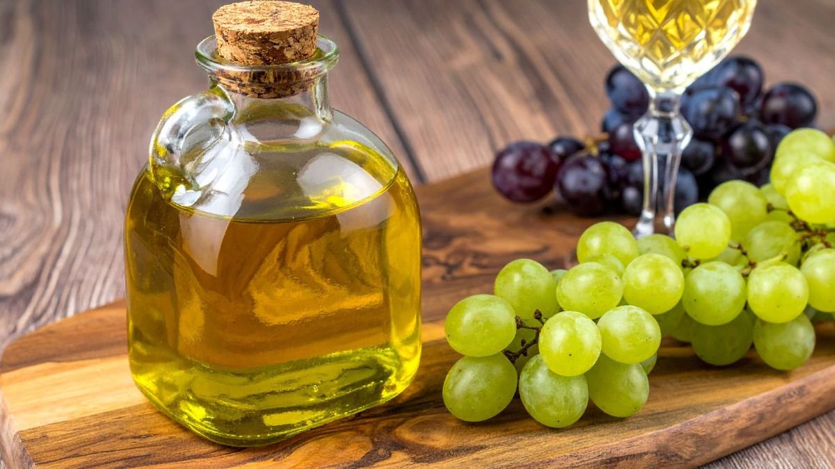 Eine Flasche Traubenkernöl steht neben frischen grünen und roten Trauben auf einem Holzbrett.
