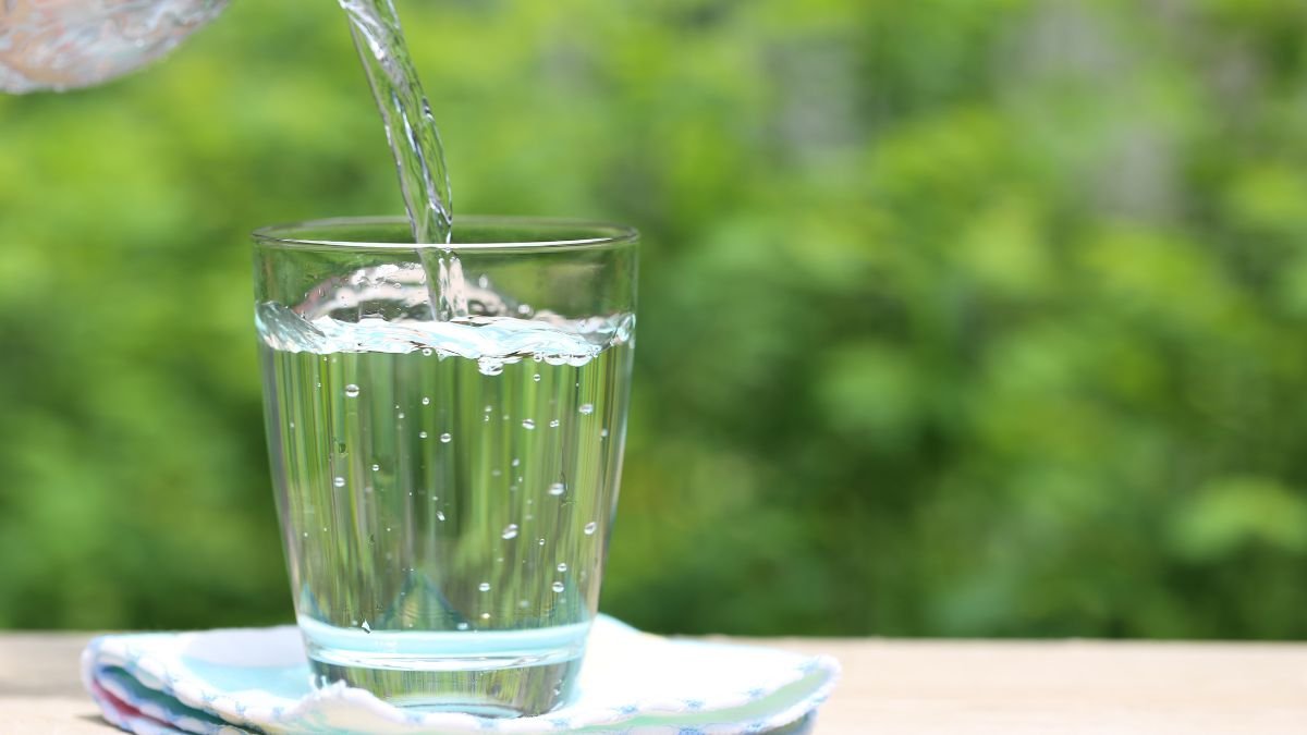Ein Glas mit destilliertem Wasser wird gefüllt, umgeben von grüner Natur.