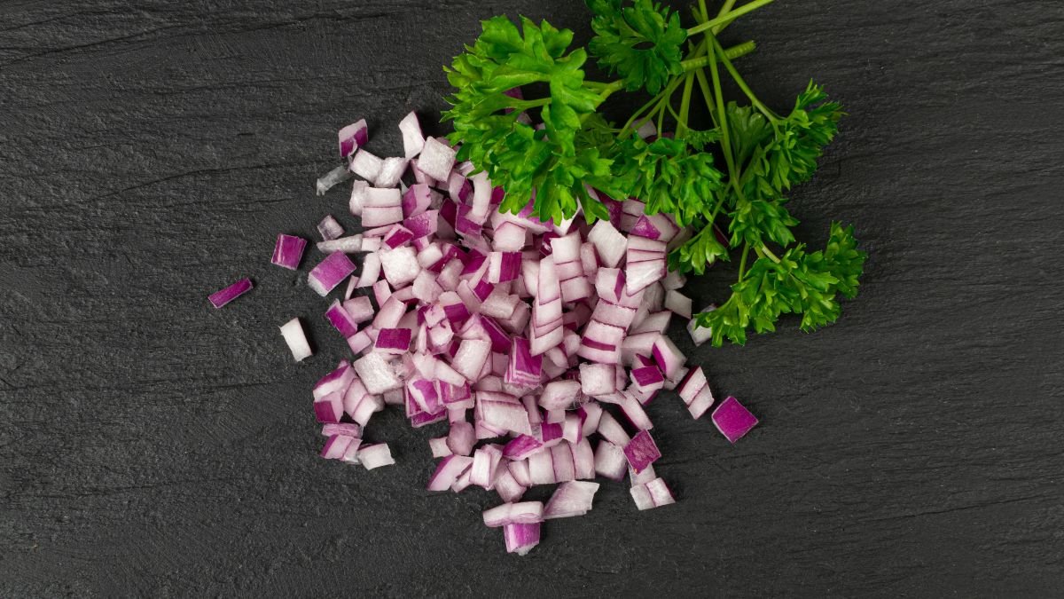 Fein gehackte rote Zwiebeln und frische Petersilie auf einem dunklen Untergrund.