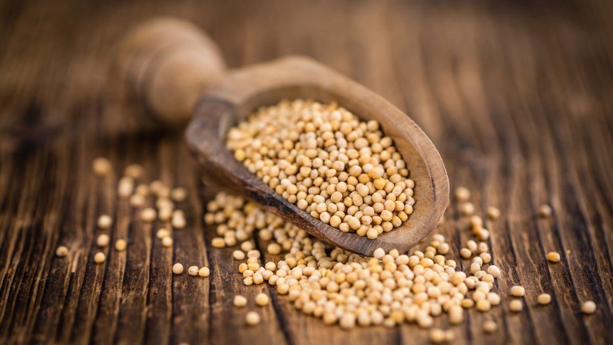 Ein Holzlöffel mit Senfkörnern auf einem rustikalen Holztisch.
