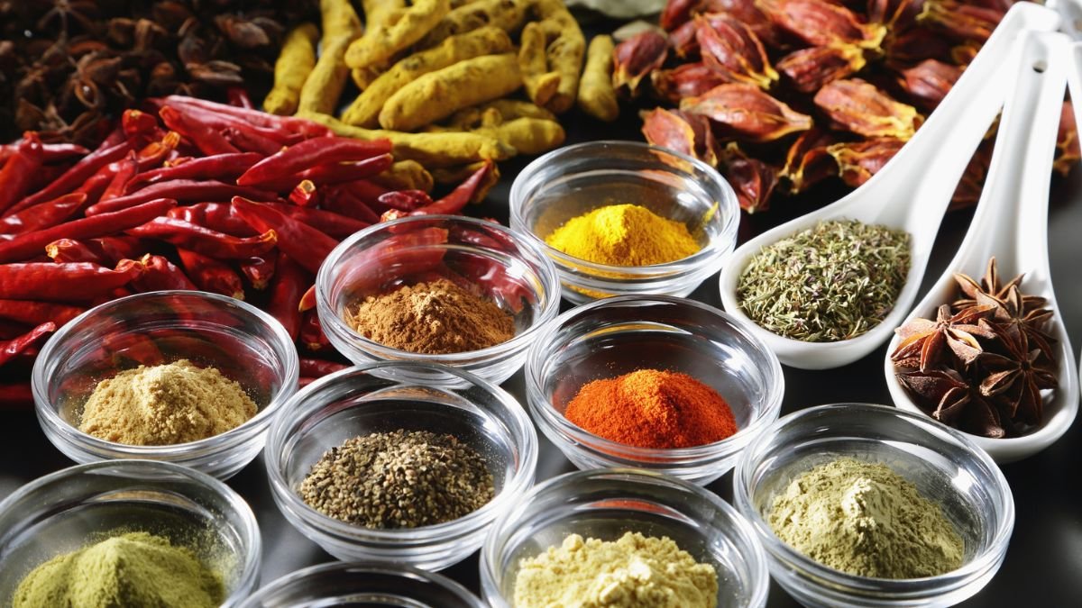 Eine Auswahl verschiedener Gewürze in Schalen, darunter Chili, Kurkuma und Kräuter.