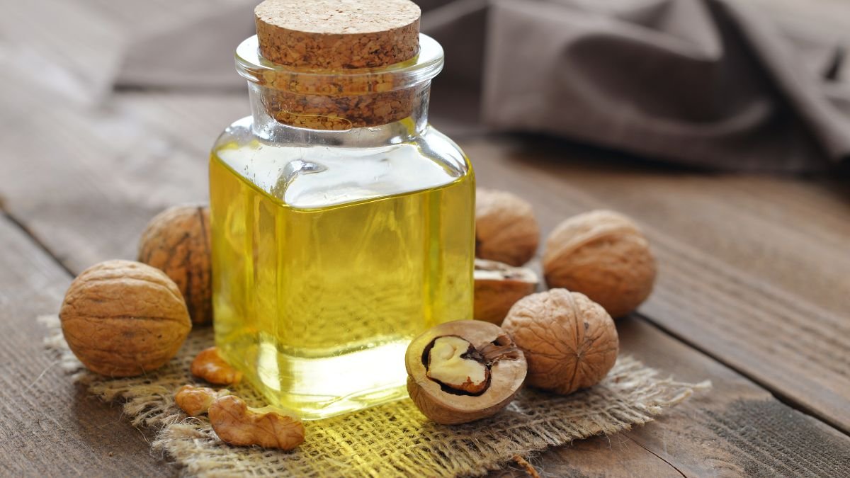 Eine Flasche Walnussöl steht neben ganzen und geschälten Walnüssen auf einem Holzuntergrund.