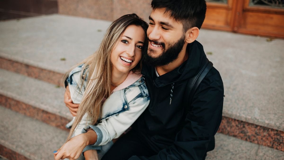 Ein lächelndes Paar sitzt auf einer Treppe und umarmt sich.