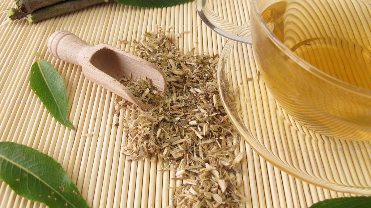 Eine Holzschaufel mit Weidenrinde neben einer Tasse Weidenrindentee auf einem Bambusuntergrund.